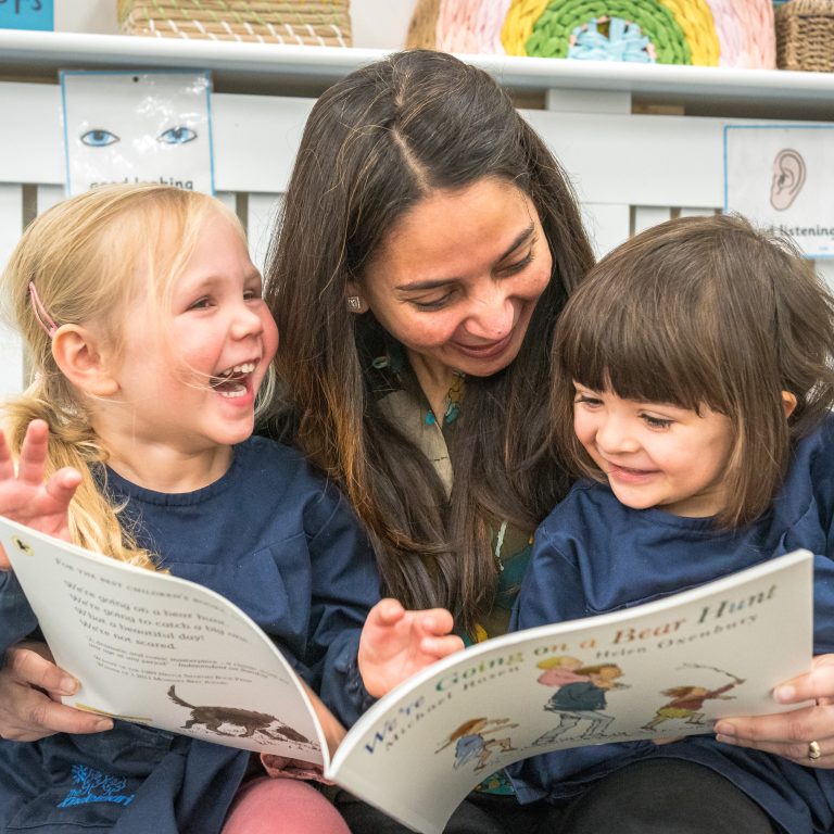 2 girls reading a book with a teacher