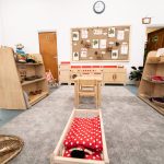 The indoor space of the nursery, featuring a wooden kitchen set up, shelves, a cot and seated areas