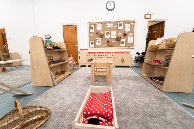 The indoor space of the nursery, featuring a wooden kitchen set up, shelves, a cot and seated areas