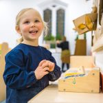 child looking up at her wooden cash register