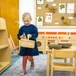 a child in a dark blue apron holding a wicker basket