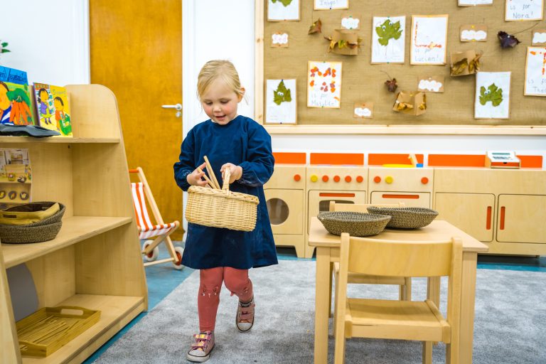 a child in a dark blue apron holding a wicker basket